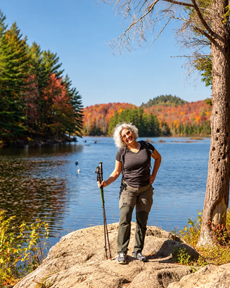 Alice com bastões de caminhada diante de um lago no Parc national du Mont-Orford durante o outono