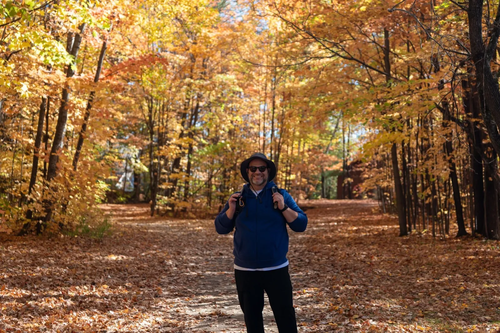Marco em uma trilha coberta por folhas de outono no Parc régional de la Rivière-du-Nord